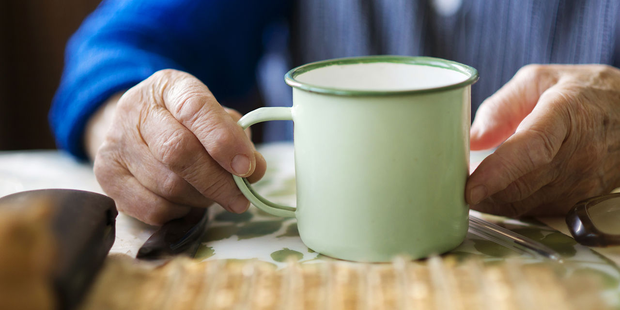 Hendene til en eldre person holder på en lysegrønn kopp