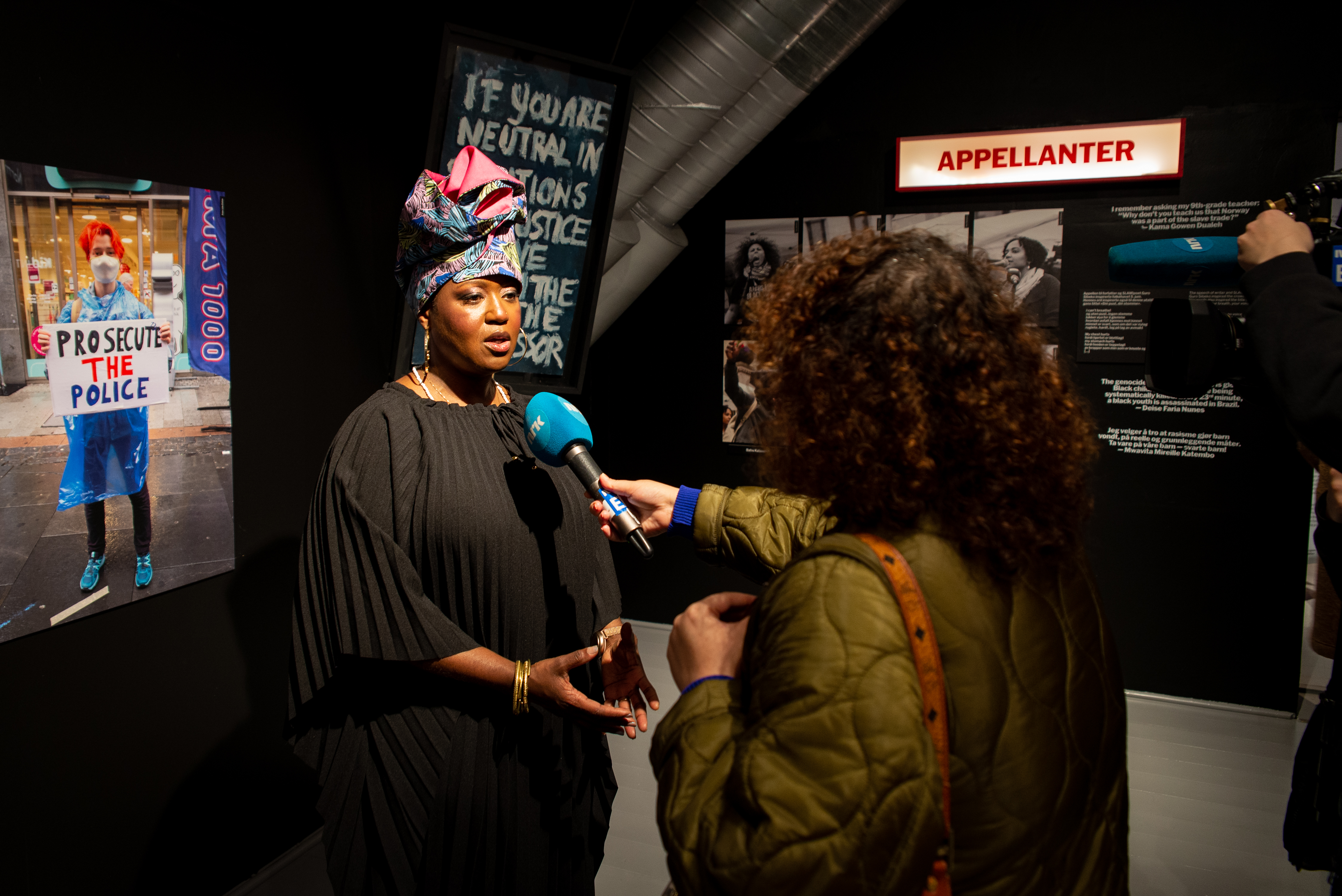 Journalist fra NRK holder en blå mikrofon foran prosjektansvarlig Michelle Tisdel inne i utstillingen Din pust, din stemme på Bymuseet i Frognerparken.