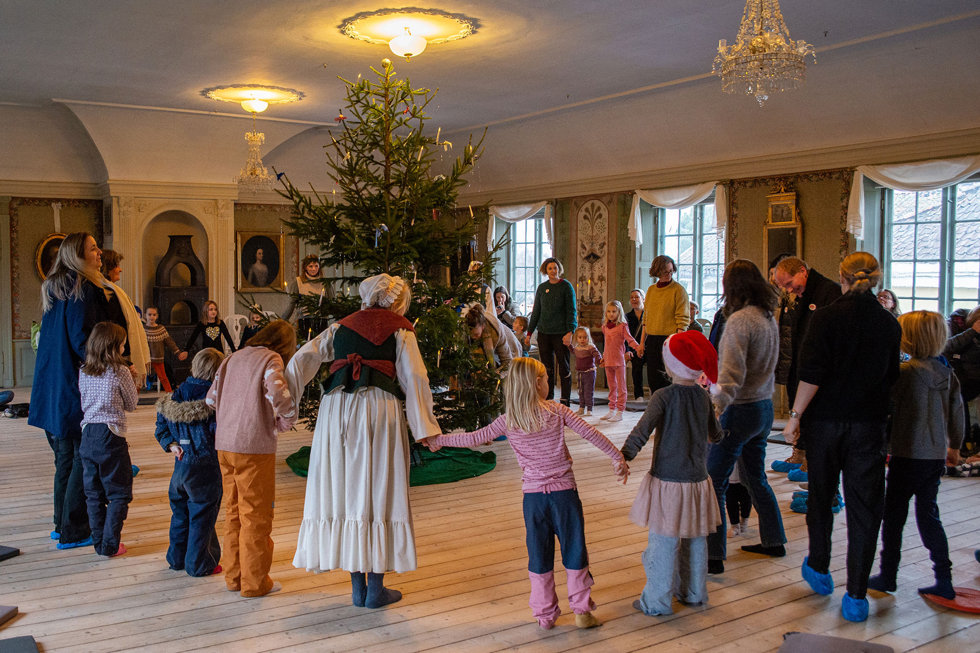 Barn og voksne går rundt et juletre. Mange har blå skoposer på.