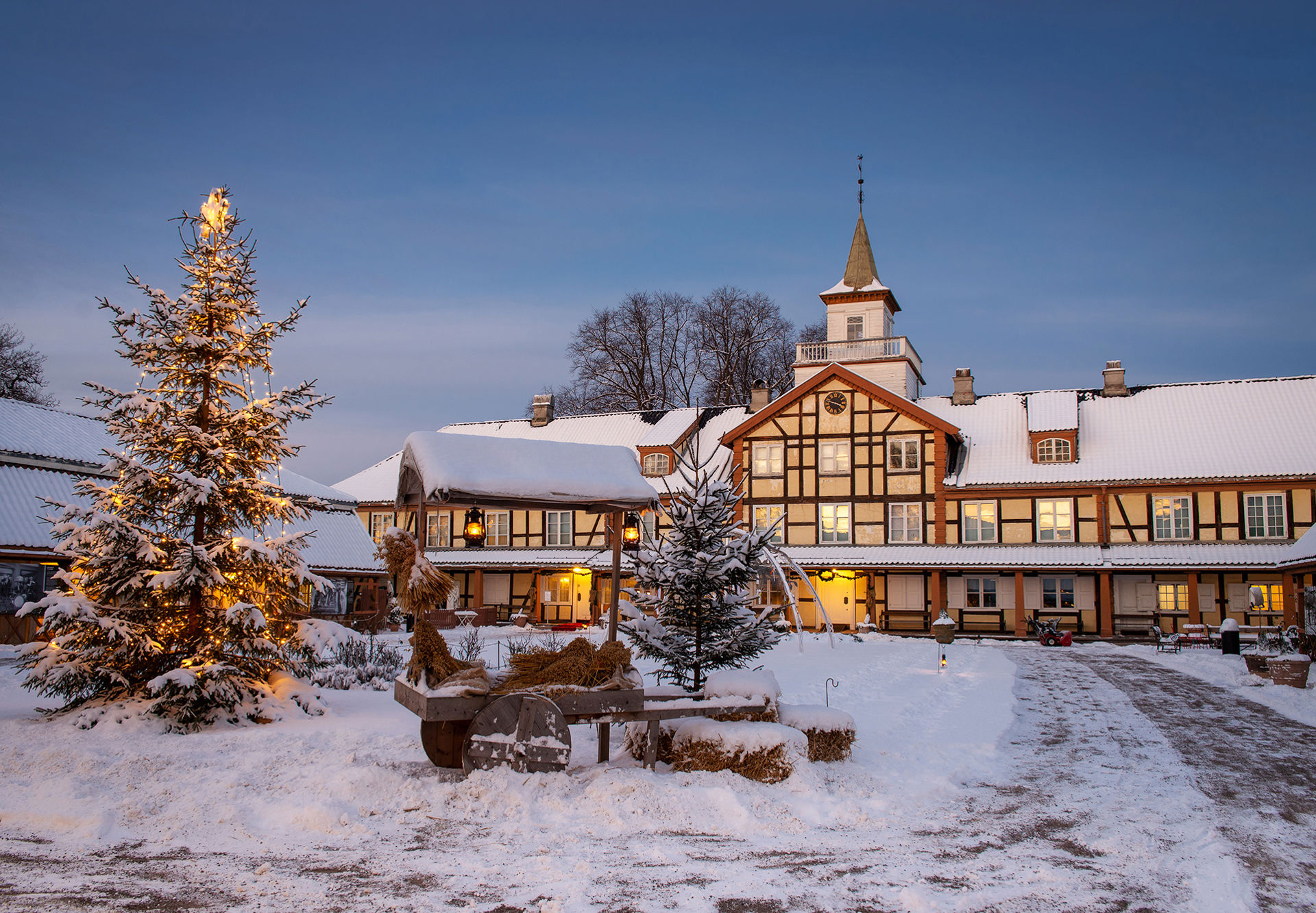 Gammel herregård med stort tun foran. Hvit snø på taket og på tunet foran. Juletre og vogn med julenek i forgrunnen.
