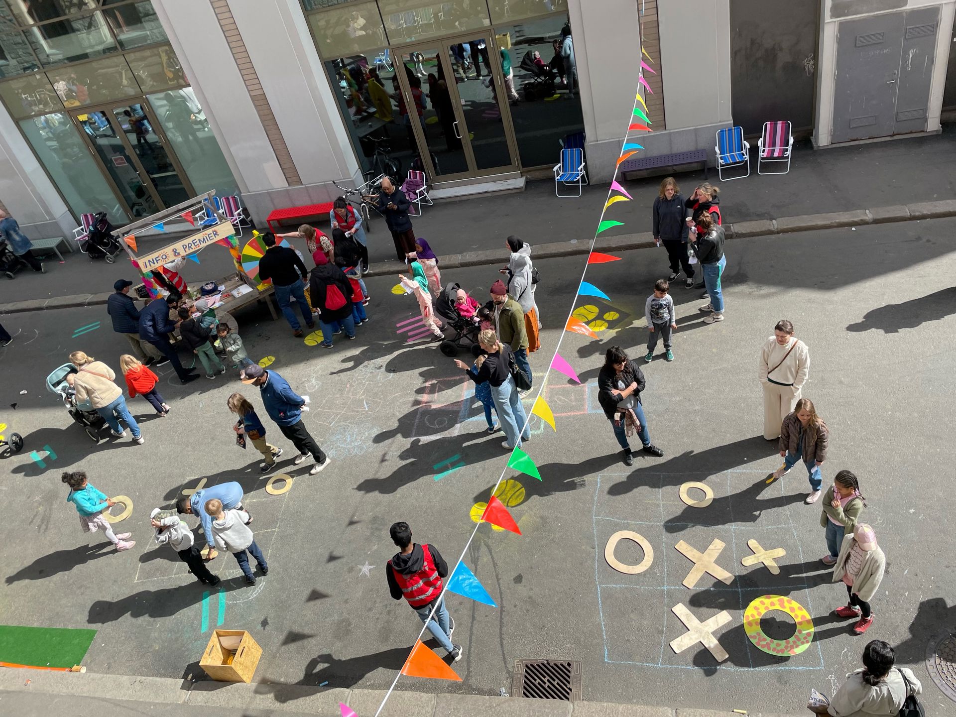 Barn og voksne leker i gaten foran Interkulturelt Museum. Fargerike vimpler henger over gaten, det er kritt-tegninger på asfalten.