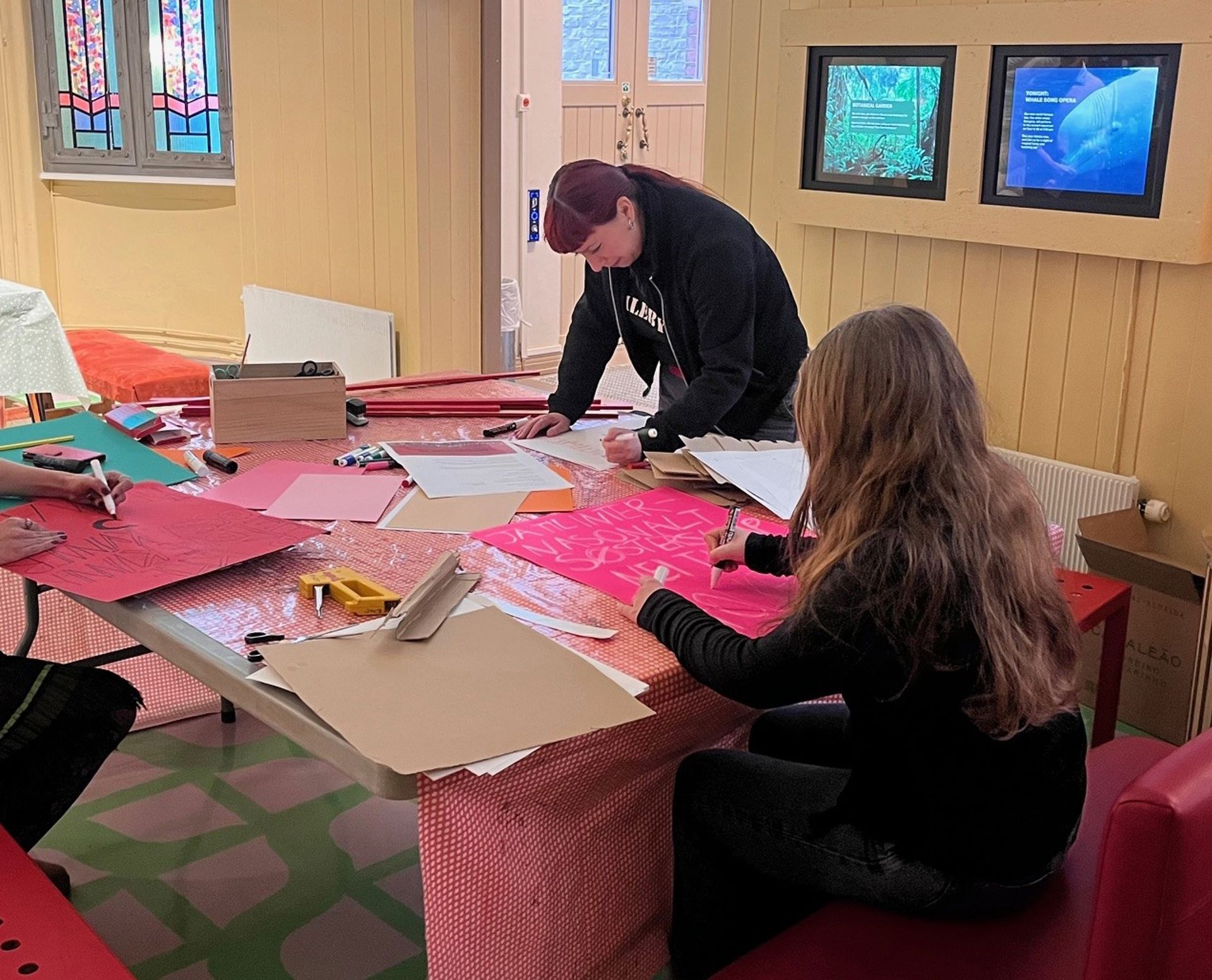 To kvinner ved et bord skriver på store rosa plakater