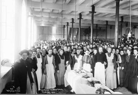 sorthvitt-bilde av kvinnelige arbeidere i forklær på en fabrikk