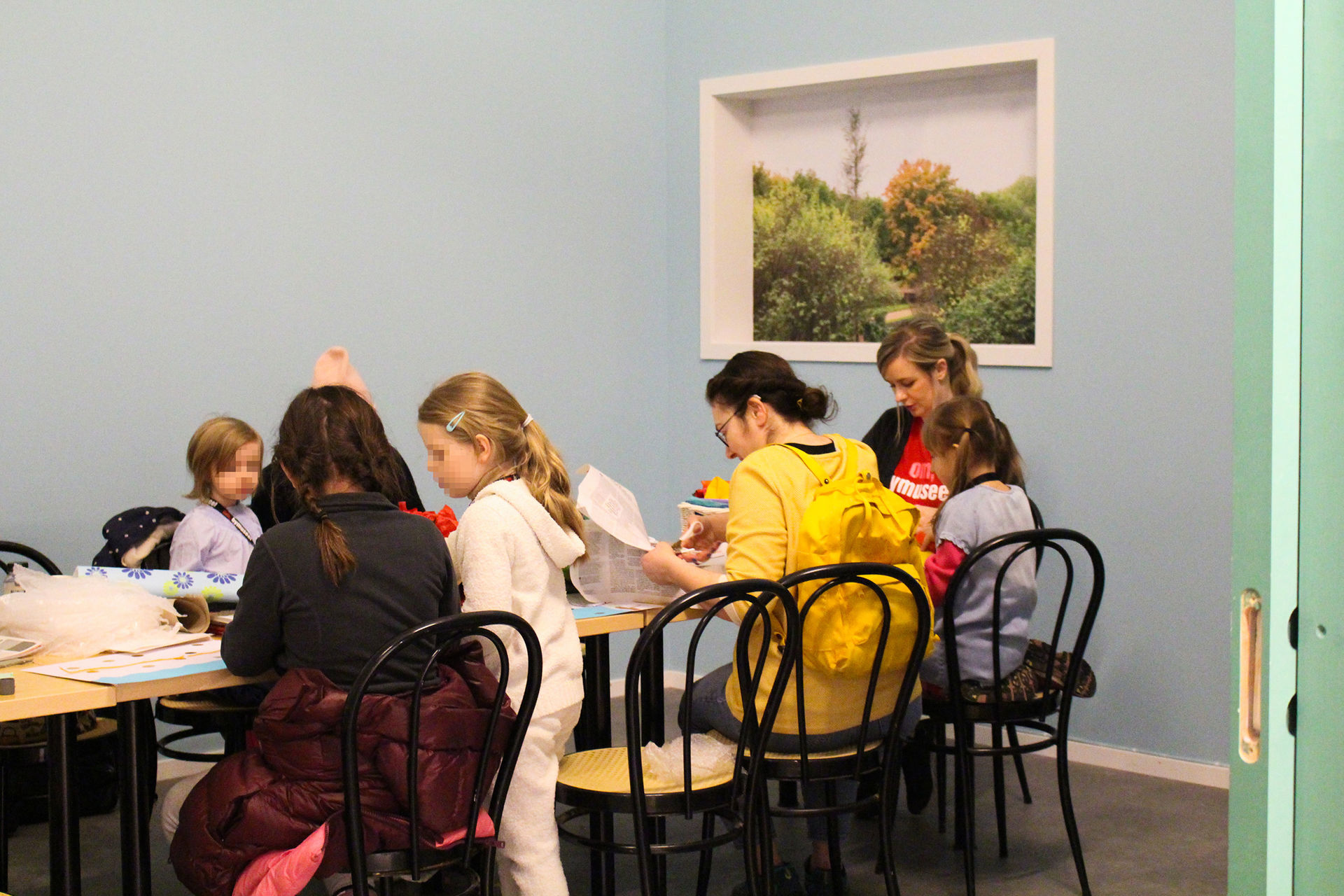 Flere barn sitter ved et bord og klipper og limer.