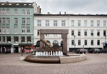 fontene og skulptur av en hånd som peker nedover midt på en brosteinlagt plass