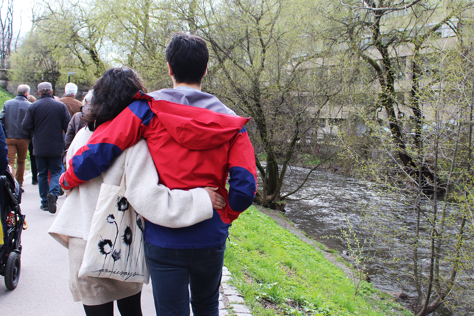 Vi ser ryggen til et ungt par som holder rundt hverandre. De går på en gangvei med Akerselva til høyre for seg.