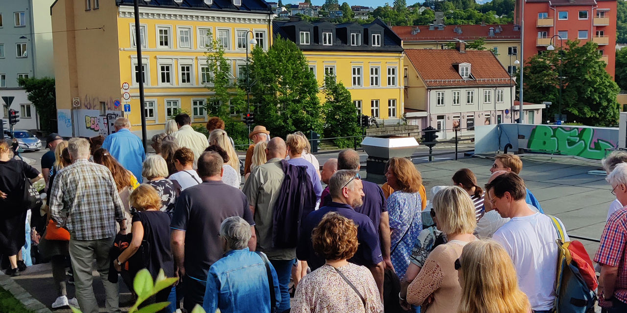 Mange mennesker på byvandring. Sol og fint vær. Fargerike murbygg i bakgrunnen.