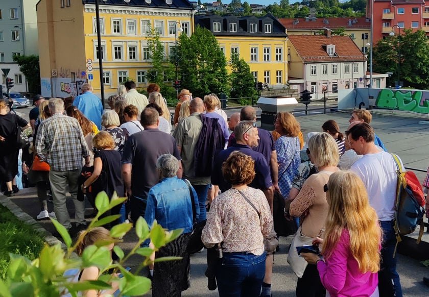 Mange mennesker på byvandring. Sol og fint vær. Fargerike murbygg i bakgrunnen.