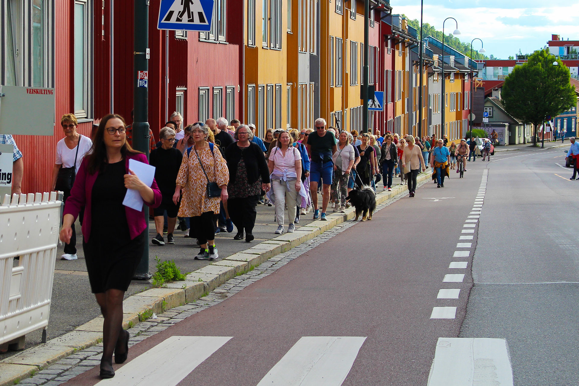 Mange mennesker på byvandring går på fortauet foran fargerike bygg.