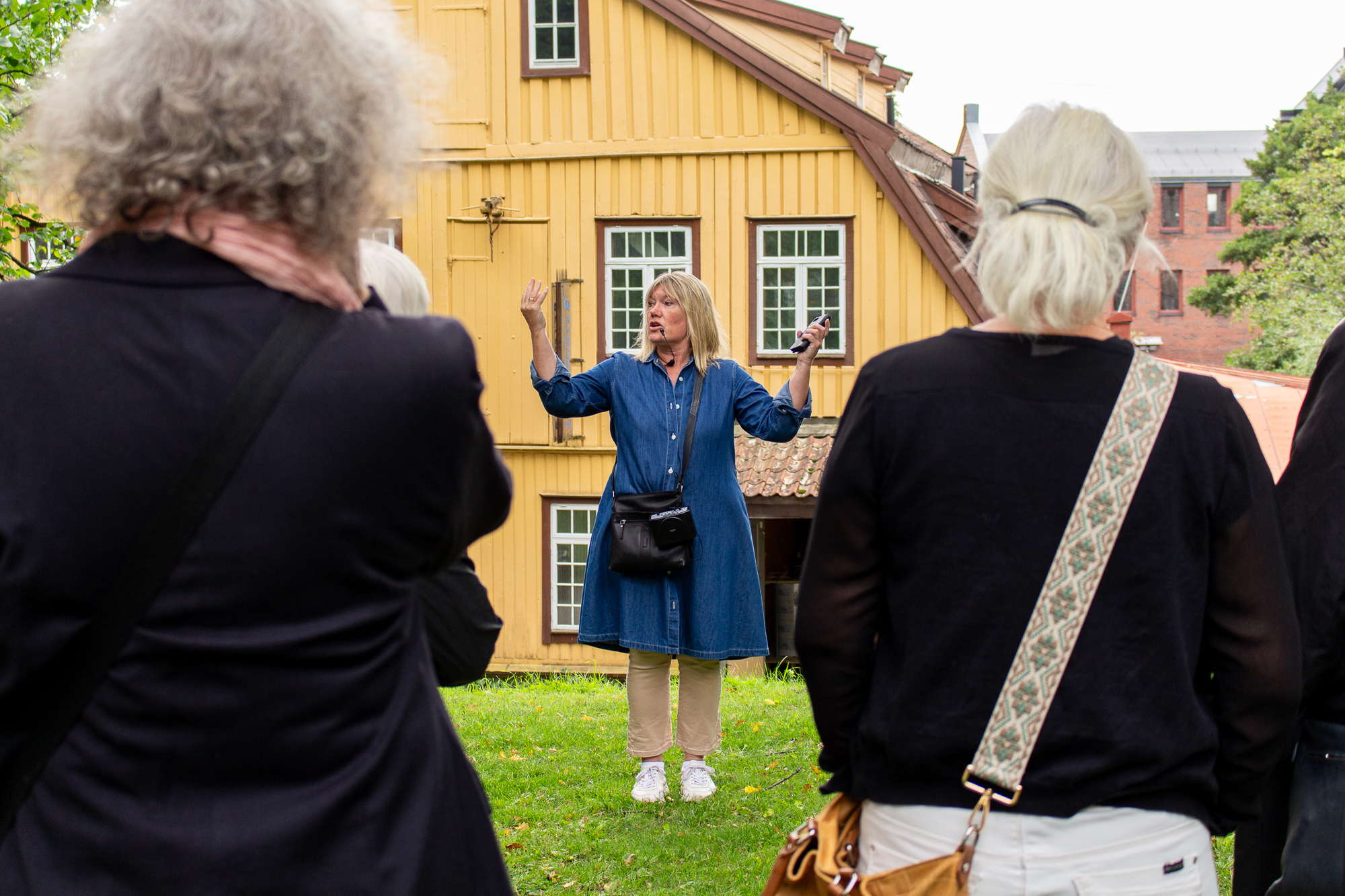 En guide snakker til tilhørere. I bakgrunnen et stort gult trebygg.