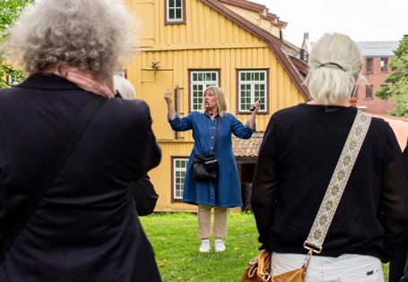 En guide snakker til tilhørere. I bakgrunnen et stort gult trebygg.