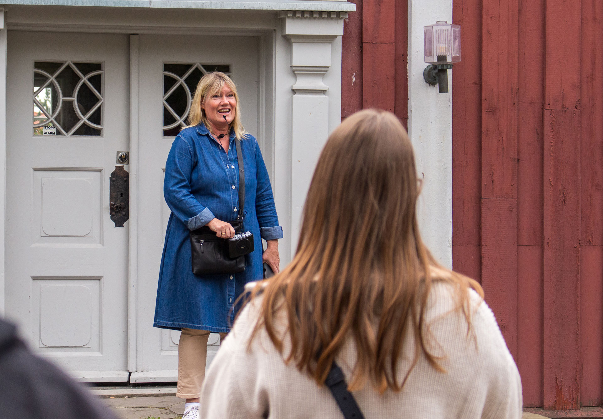 En guide står på trammen til et gammelt rødt hus.