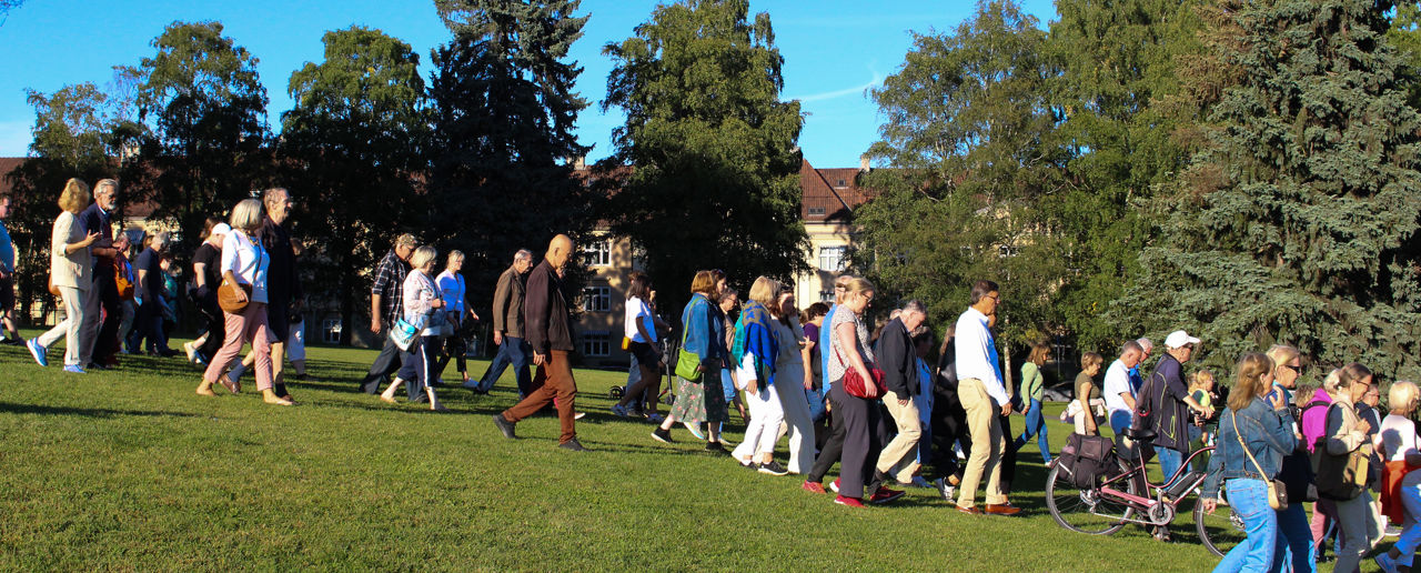 Mange personer går nedover en grønn slette med trær og blå himmel i bakgrunnen