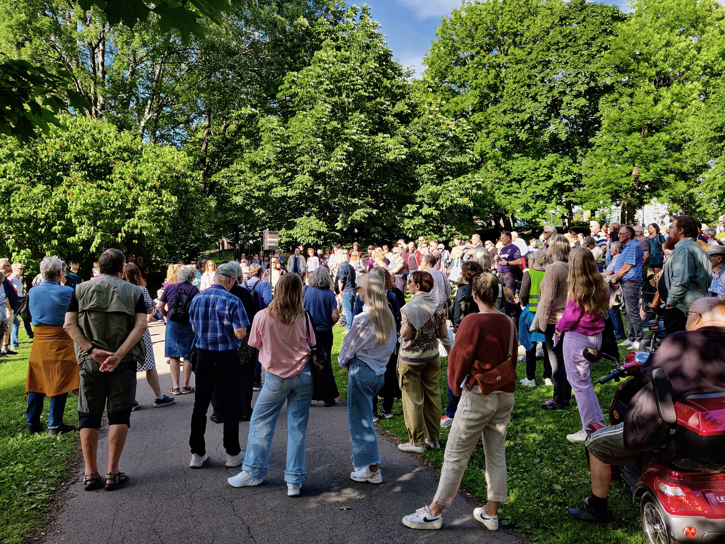 Folkemengde i en park samlet rundt en person som snakker i en mikrofon