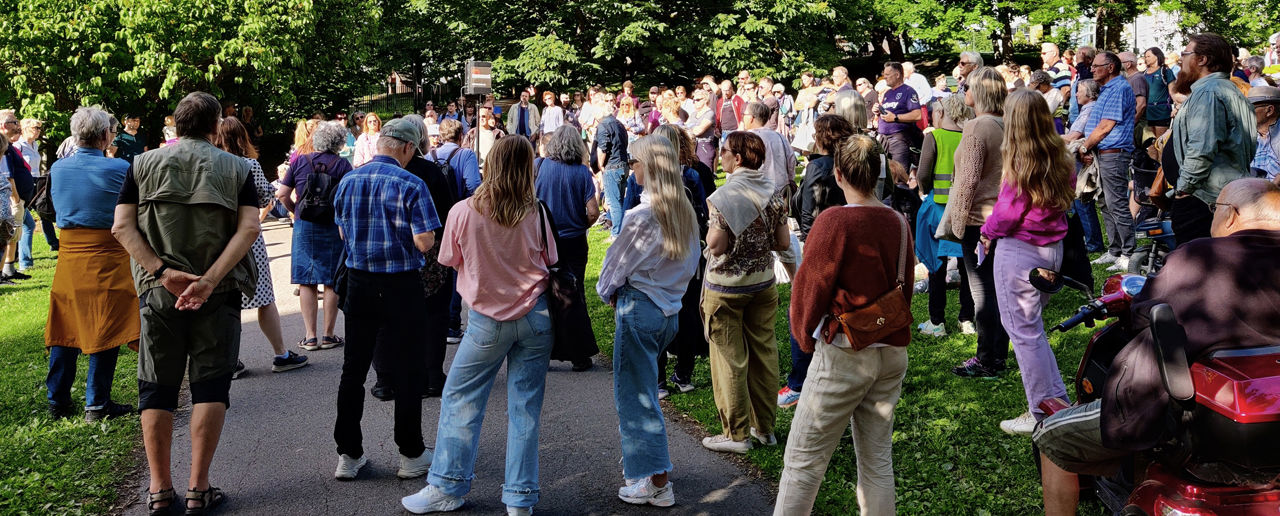 Folkemengde i en park samlet rundt en person som snakker i en mikrofon
