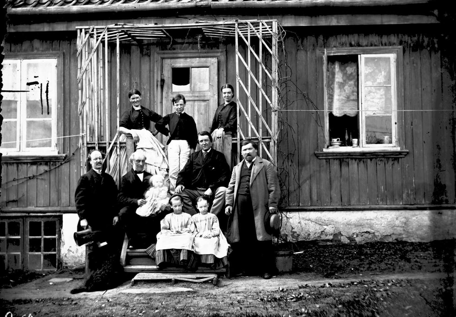 Syv voksne og tre barn på trappen inn til et gammelt trehus