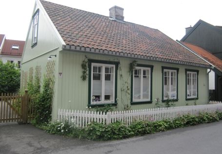 Lysegrønt trehus med mørkegrønne sprosser, rødt tak, hvitt stakittgjerde