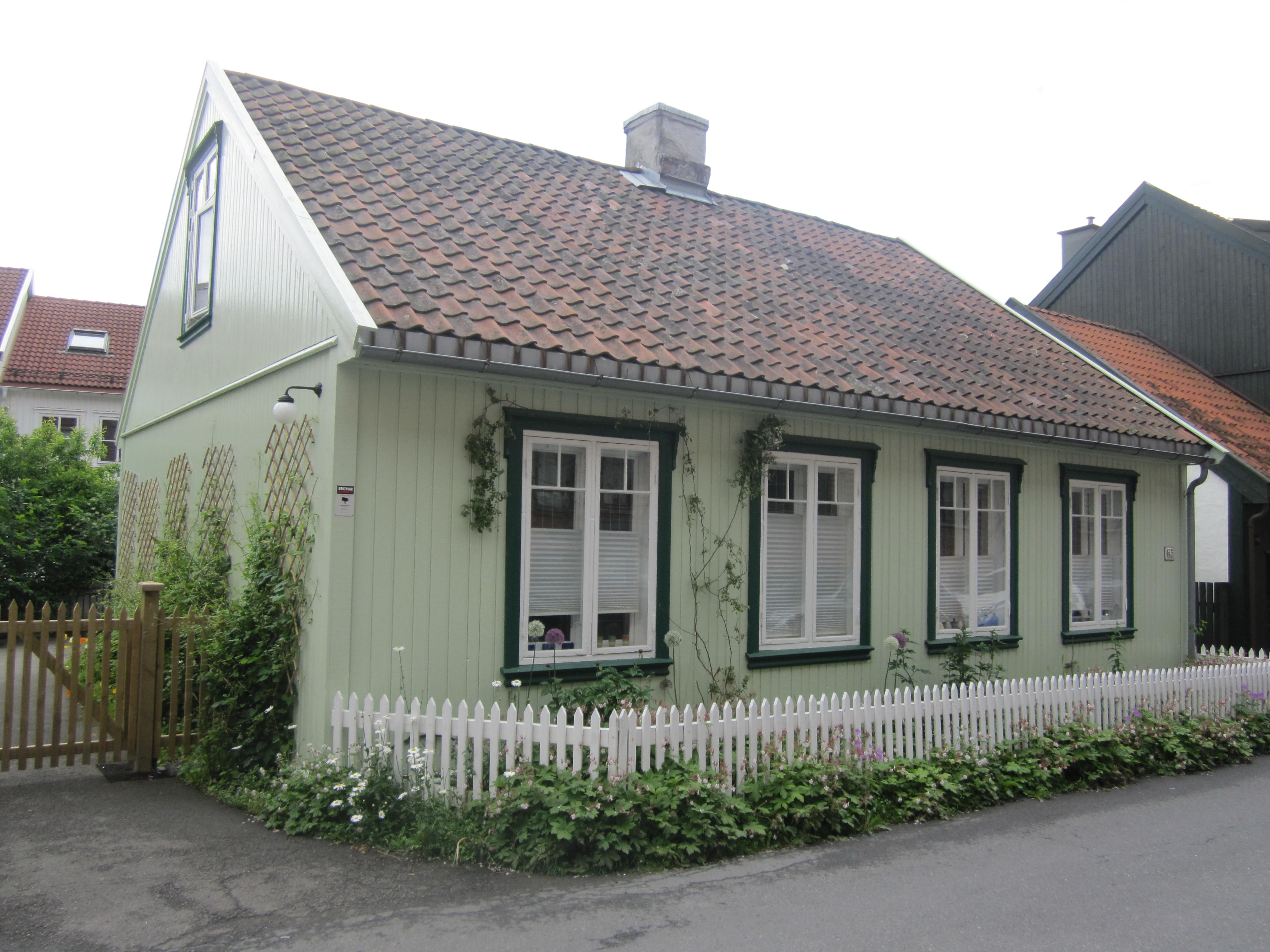 Lysegrønt trehus med mørkegrønne sprosser, rødt tak, hvitt stakittgjerde