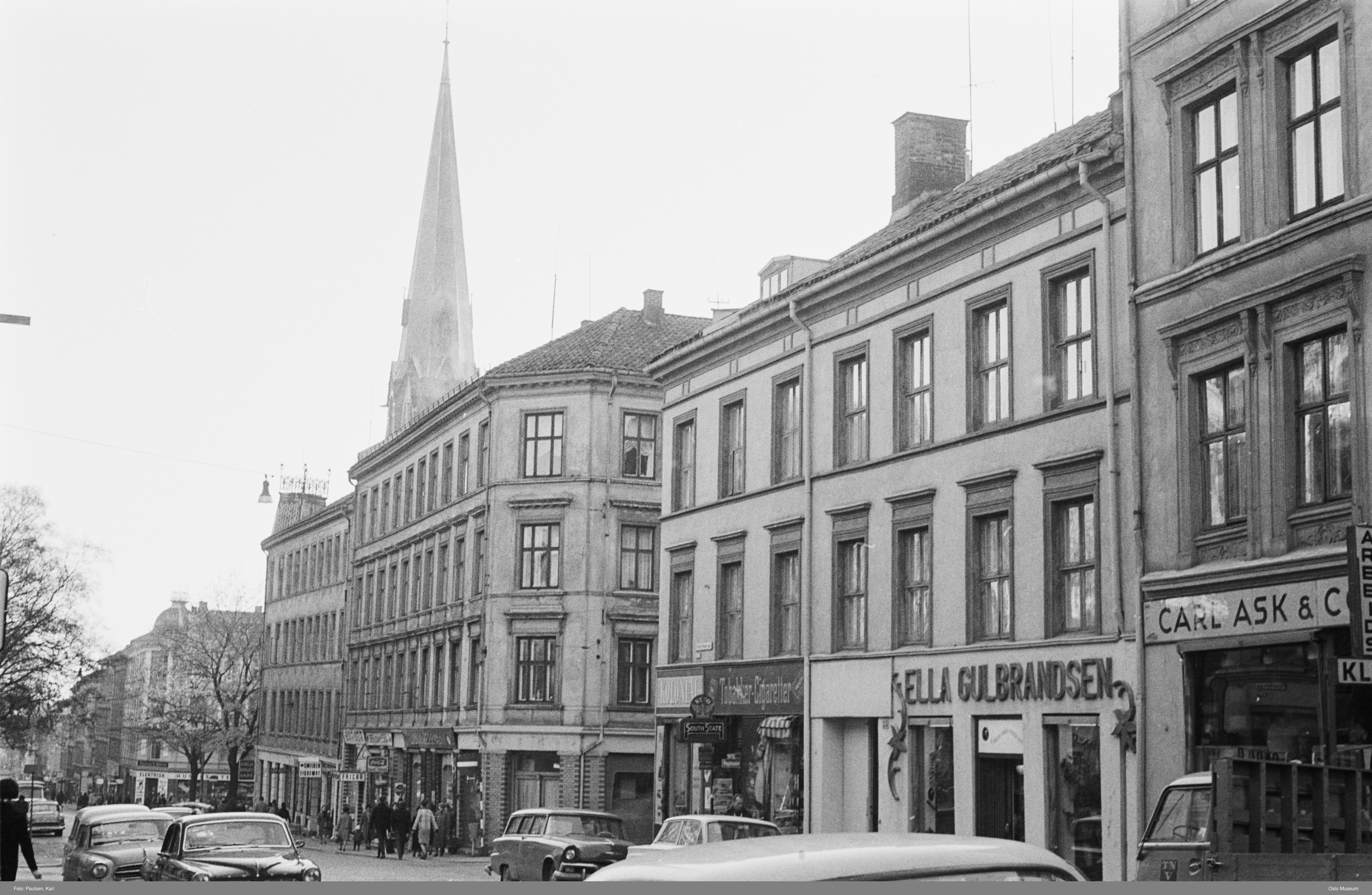 Sorthvitt-bilde av Grünerløkka, boligbygg nedover en gate med biler og mennesker, kirkespir i bakgrunnen