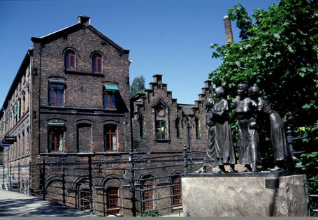 Stort murbygg i bakgrunnen og skulptur av fire arbeiderjenter