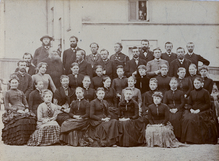 Kvinner og menn oppstilt på fem rader til et gruppebilde fra 1885. De fleste har seriøse blikk rettet mot kamera.