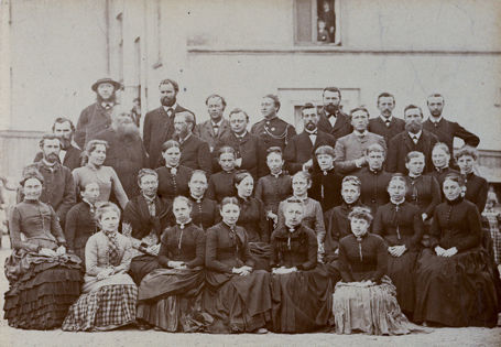 Kvinner og menn oppstilt på fem rader til et gruppebilde fra 1885. De fleste har seriøse blikk rettet mot kamera.