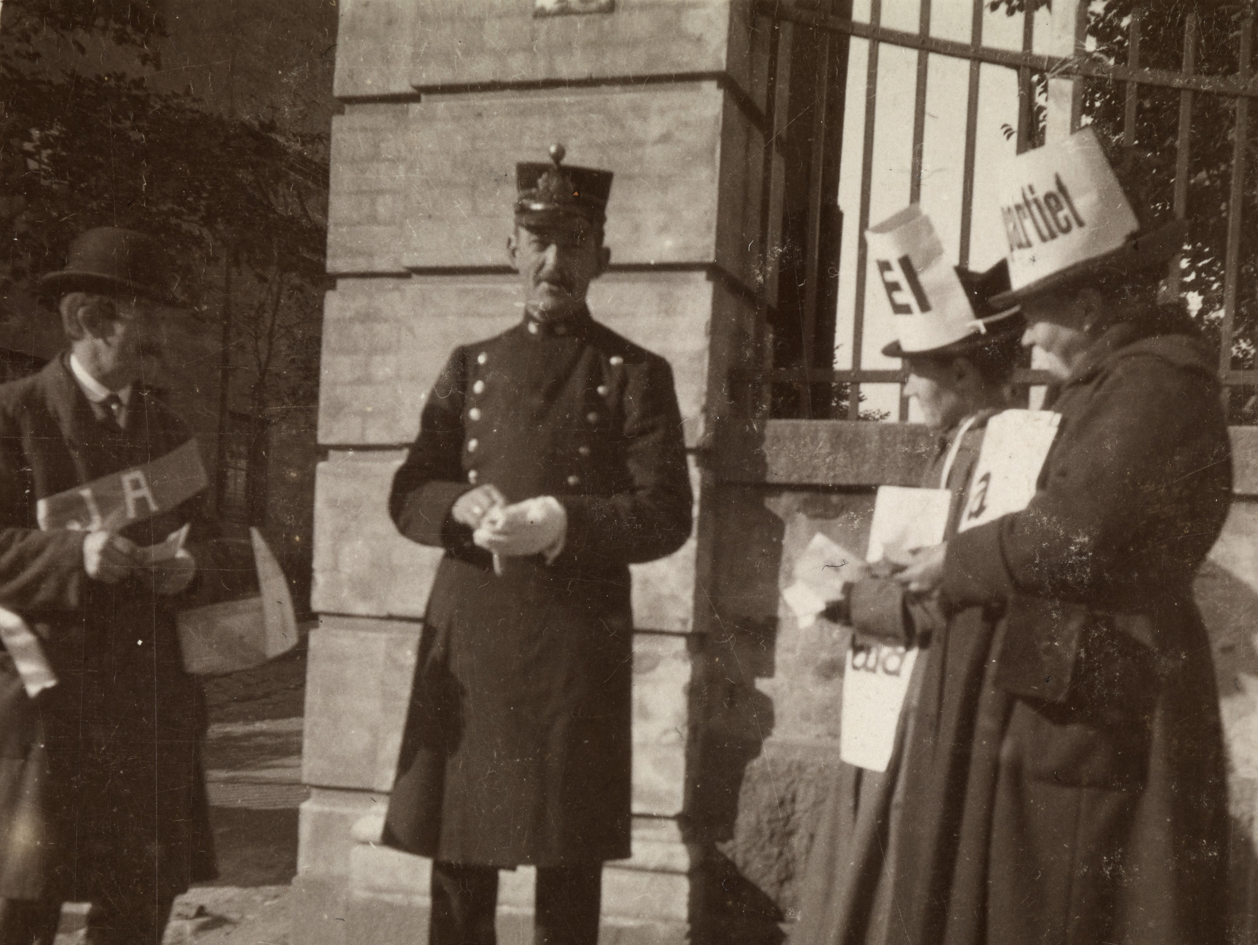 Tre personer står utenfor en bygning, med en uniformert politimann i midten og personer med plakater på hver side