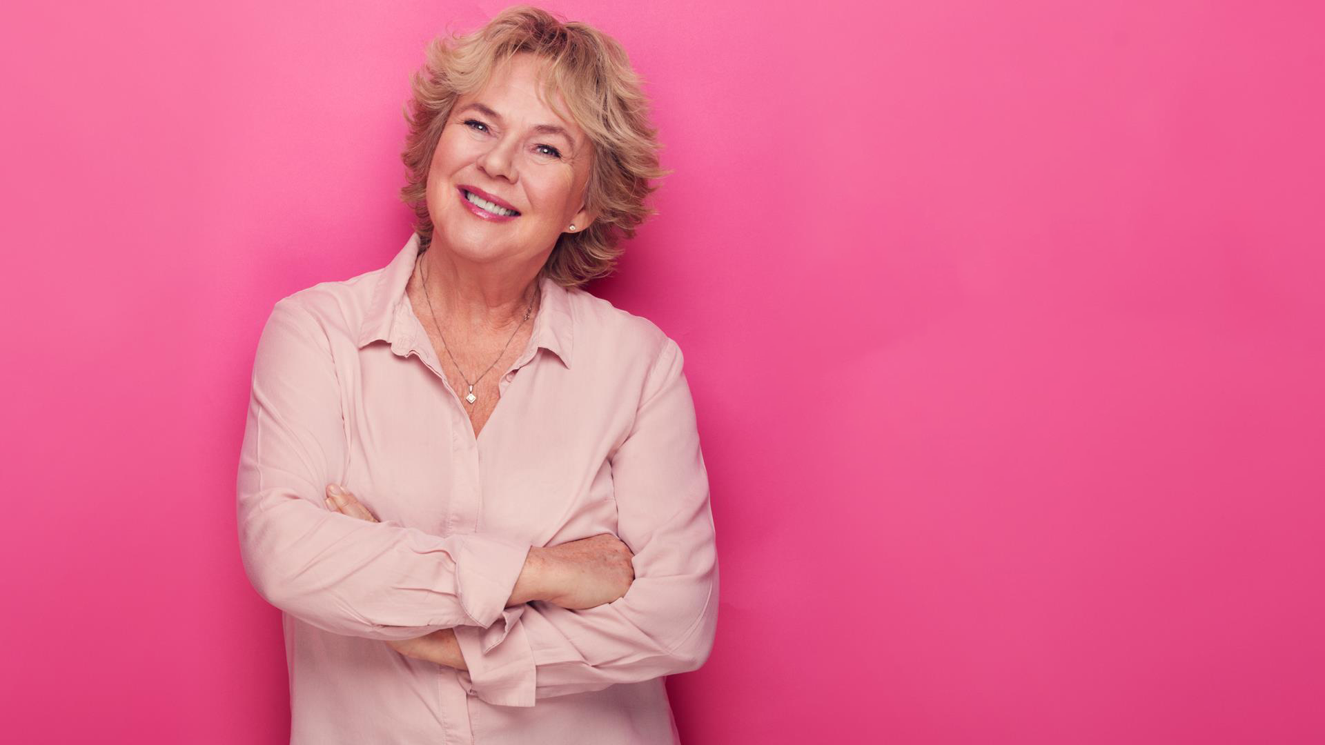 Kari-Ann Grønsund smilende med armene i kors foran en knall rosa vegg