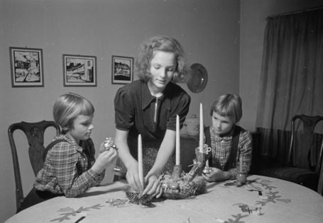 kvinne ordner på lysestake med to yngre jenter ved siden av seg