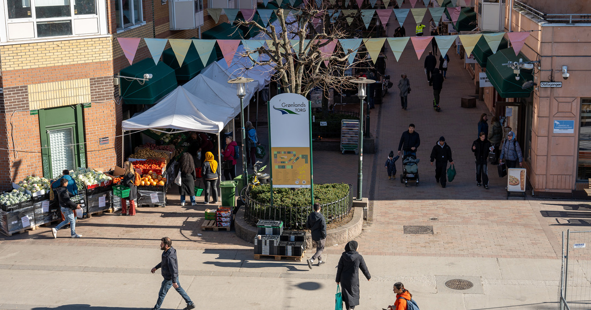oversiktsbilde over grønland torg med mennesker, grønnsaksboder og vimpler over gata
