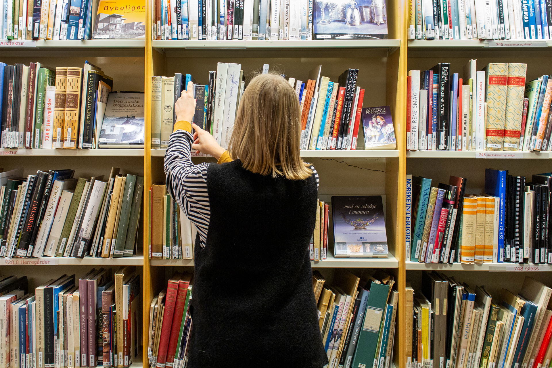 Ung kvinne ser i hyllene på  biblioteket