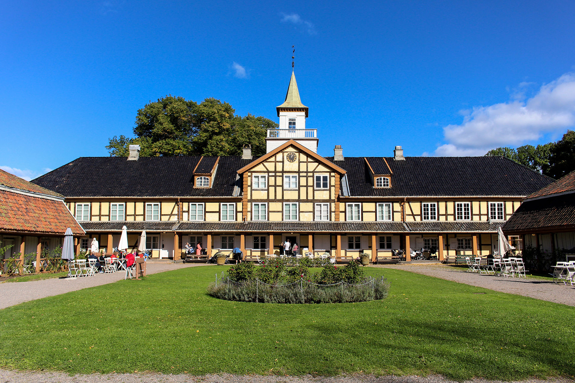 Gammelt ærverdig bygg med en grønn gressplen foran. Solskinn og fint vær.
