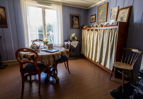 Et bord med tre stoler står midt i rommet. På de blå veggene henger bilder og malerier.
