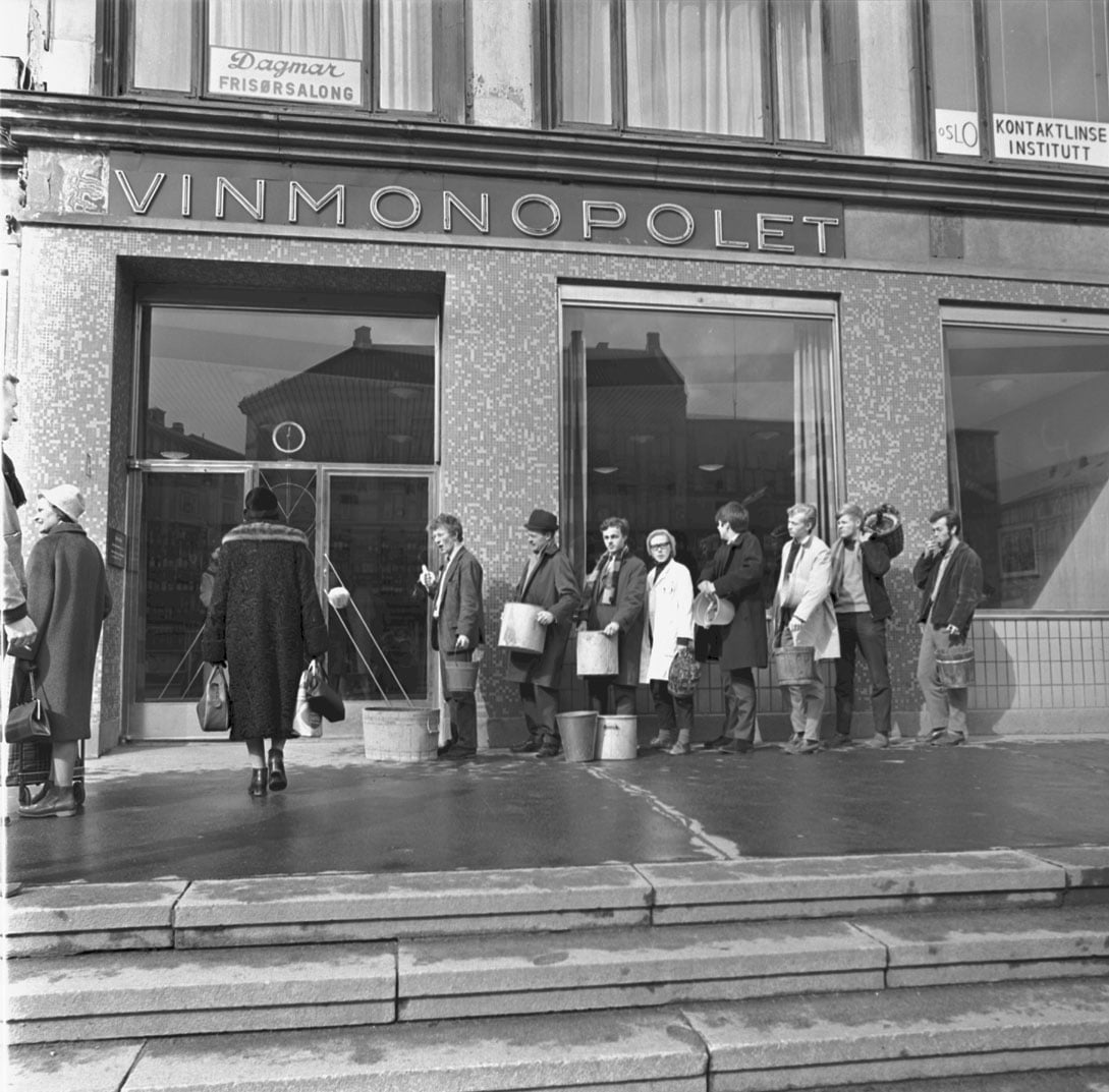 Mennesker i k&oslash; med b&oslash;tter utenfor Vinmonopolet