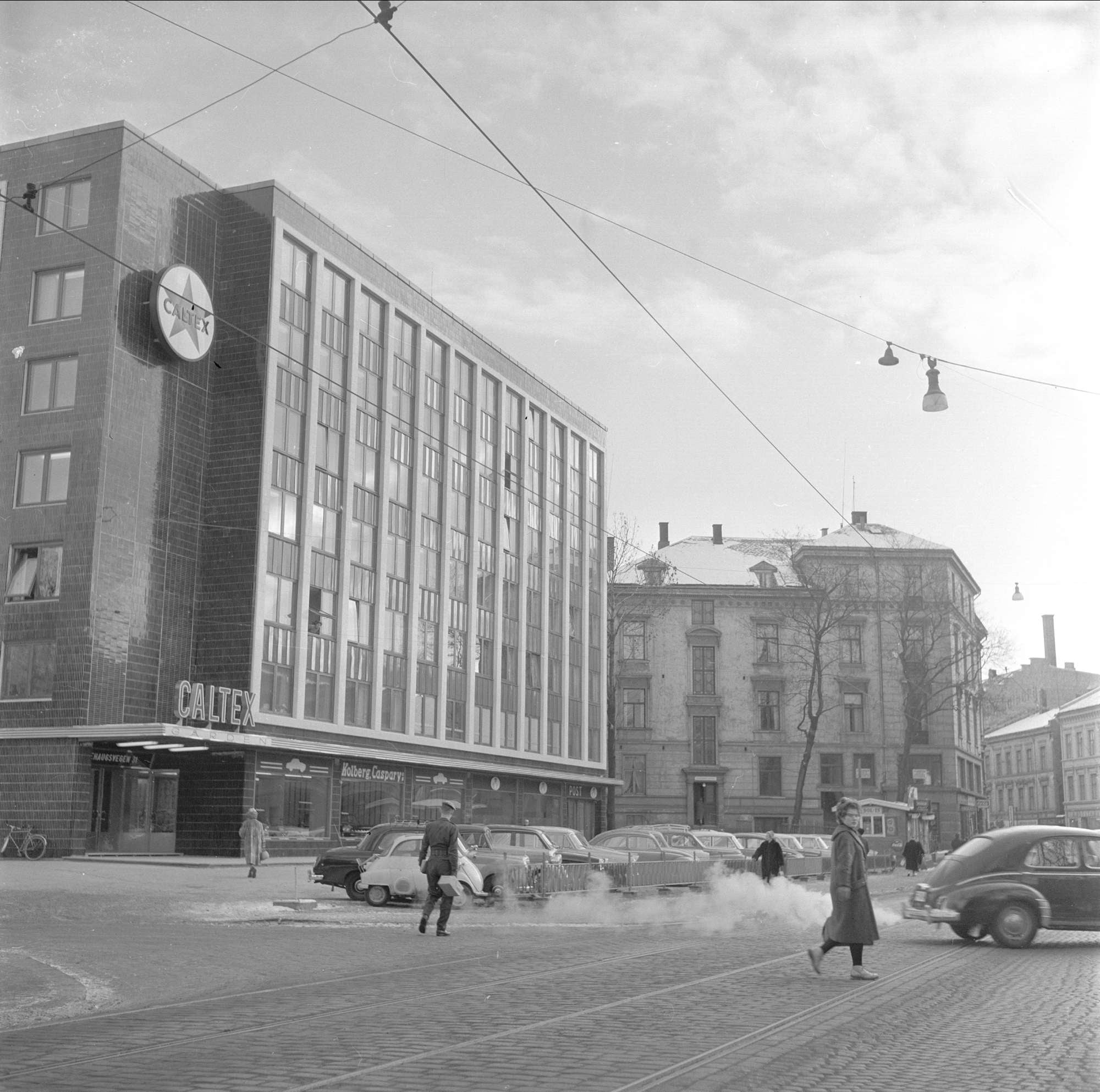 Fasadebilde av kontorbygg med skiltet Caltex og parkerte gamle biler p&aring; gata foran