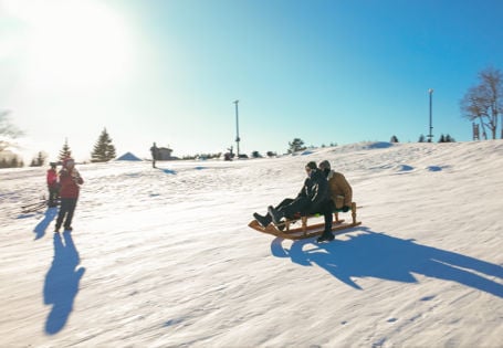 To personer på kjelke nedover snøkledd bakke