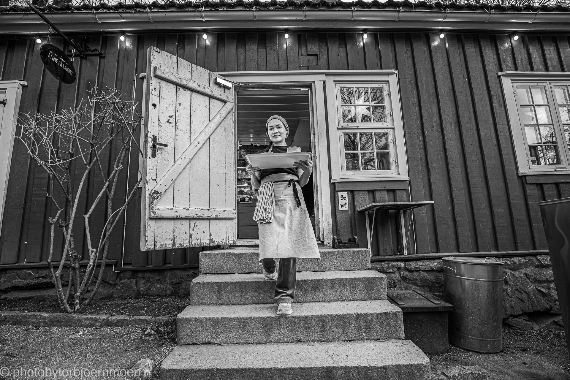kvinne i forkle går ned trapp fra gammelt hus mens hun holder et brett