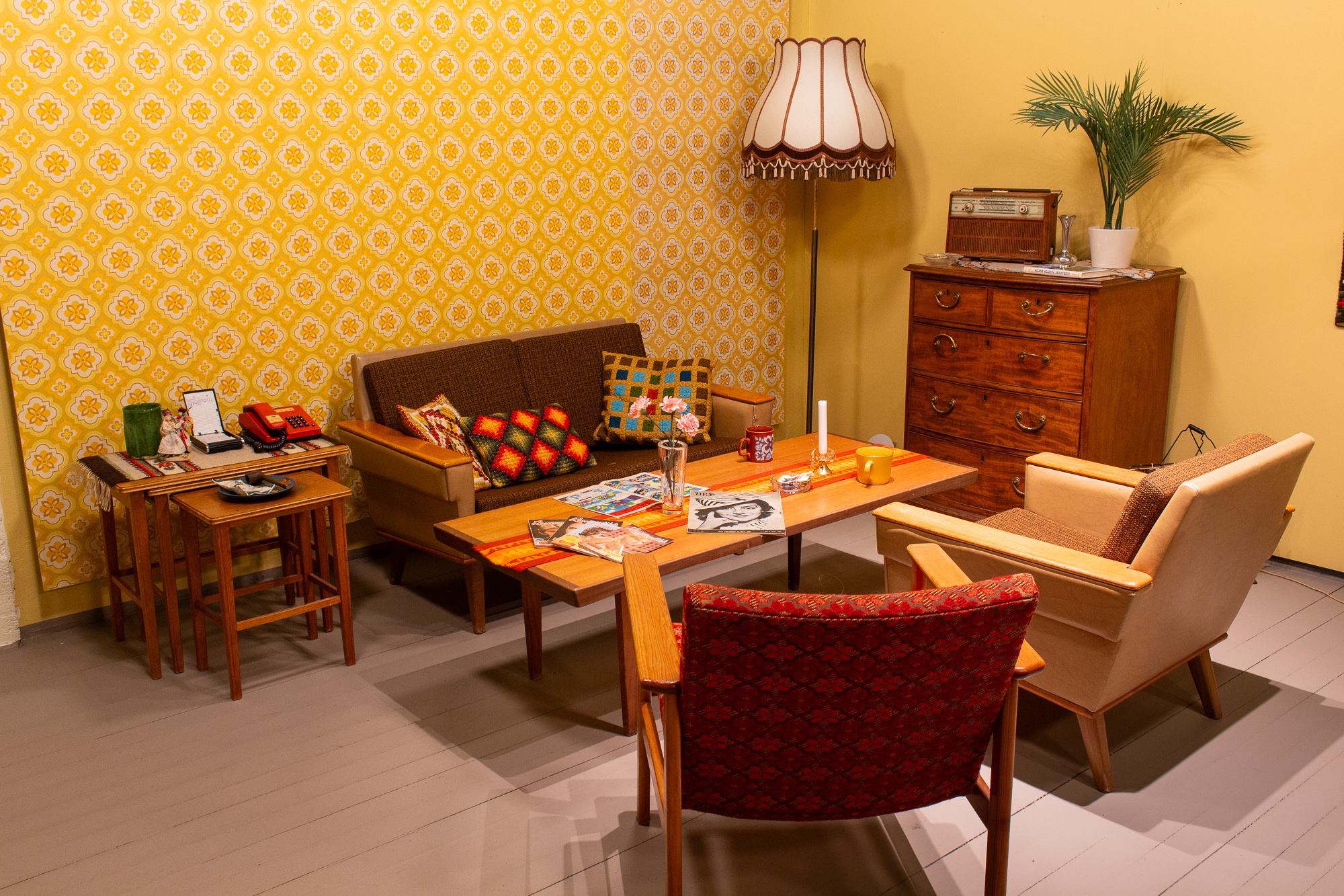 Salong med en liten sofa, to stoler, et sofabord, settebord, lampe og kommodeseksjon. Pyntegjenstander på bordene.