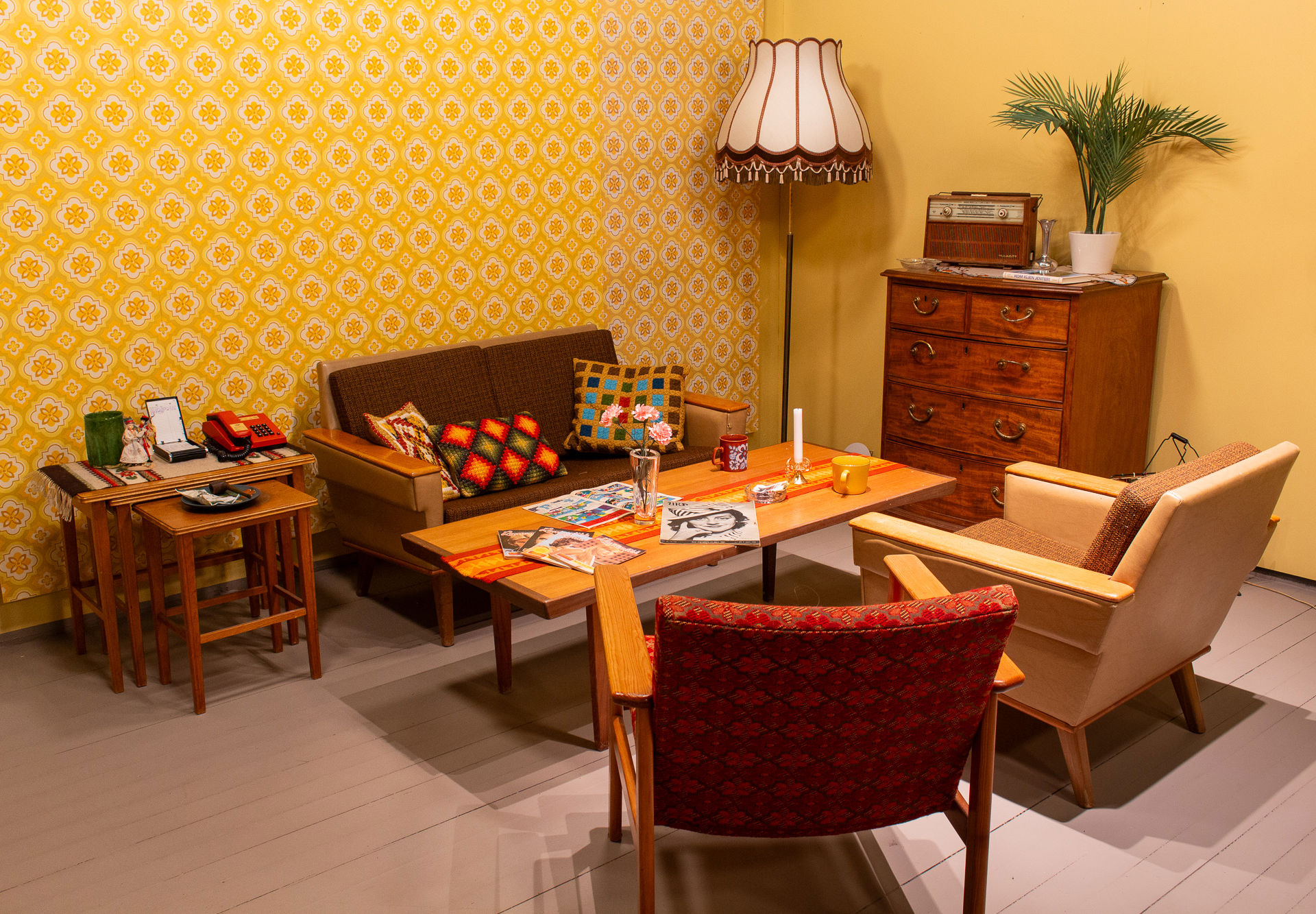 Salong med en liten sofa, to stoler, et sofabord, settebord, lampe og kommodeseksjon. Pyntegjenstander på bordene.