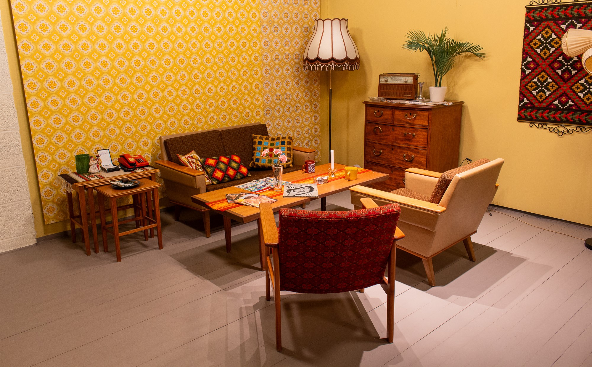 Salong med en liten sofa, to stoler, et sofabord, settebord, lampe og kommodeseksjon. Pyntegjenstander på bordene.