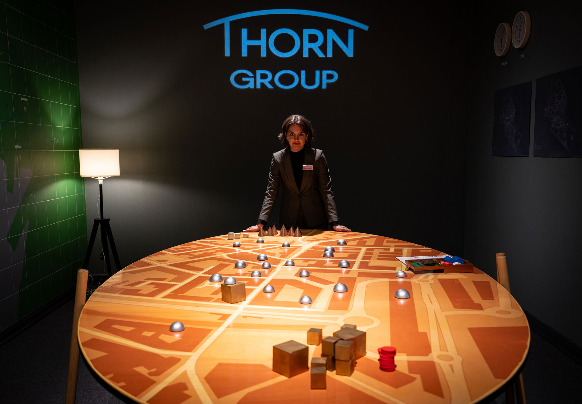 Dame i dress i et mørkt rom lener seg på et stort spillbord mens hun er i kamera. Thorn Group står i store blå bokstaver på veggen bak.