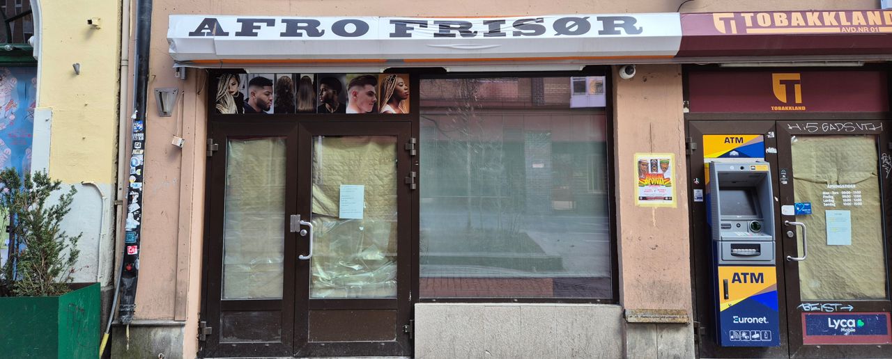 Fasade på bygg med vinduer og dører dekket av papp. Skilt med Afro Frisør.