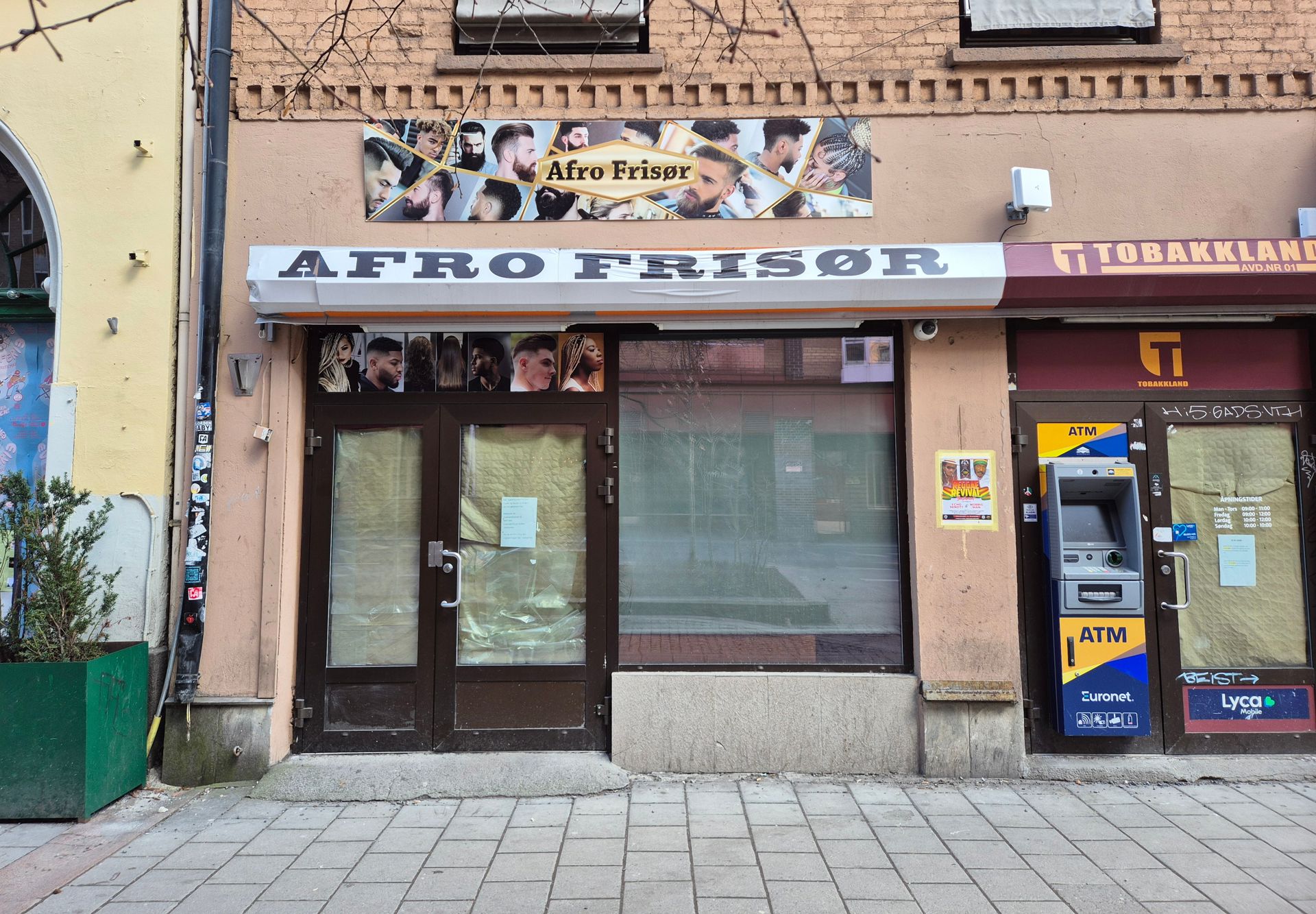 Fasade på bygg med vinduer og dører dekket av papp. Skilt med Afro Frisør.