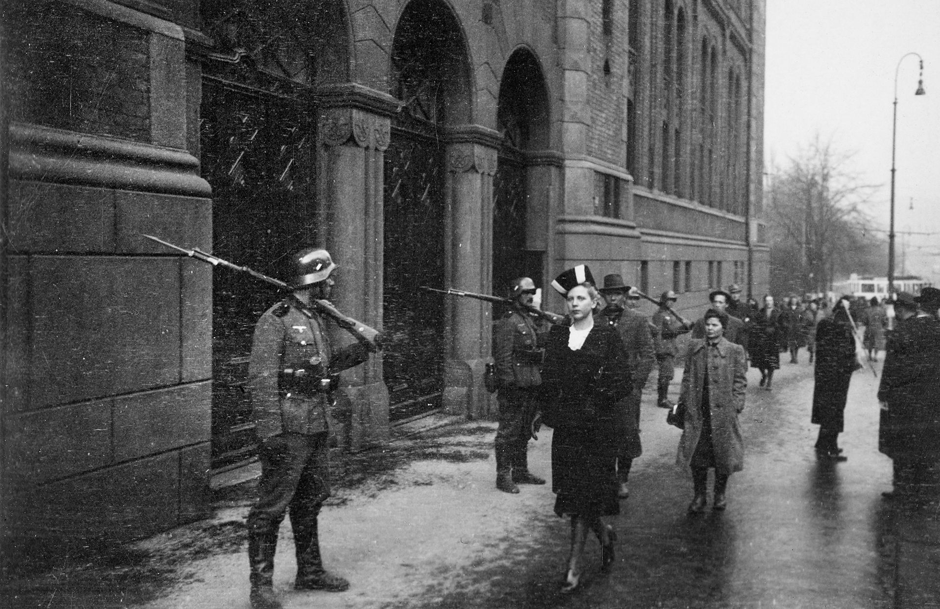 Siden av stortingsbygningen, snøvær, tyske soldater, dame med hatt passerer