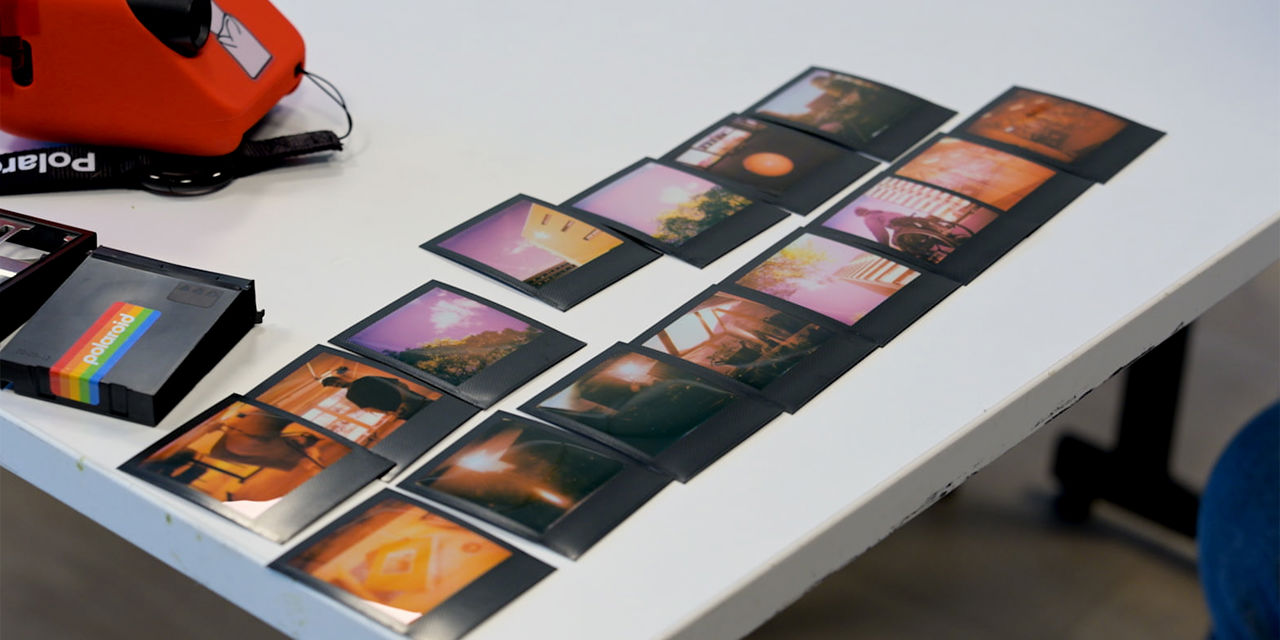 15 polaroidbilder liggende på to rader på et hvitt bord med polaroidkamera i bakgrunnen.