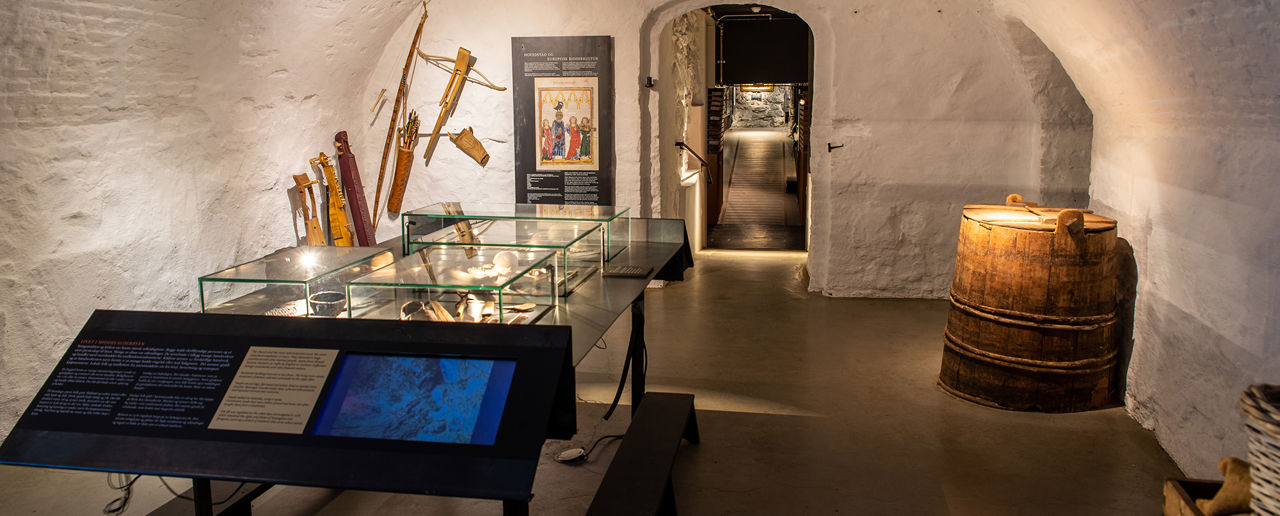 Kjellerlokale i et museum, hvitmalte murvegger og et glassmonter med museumsgjenstander