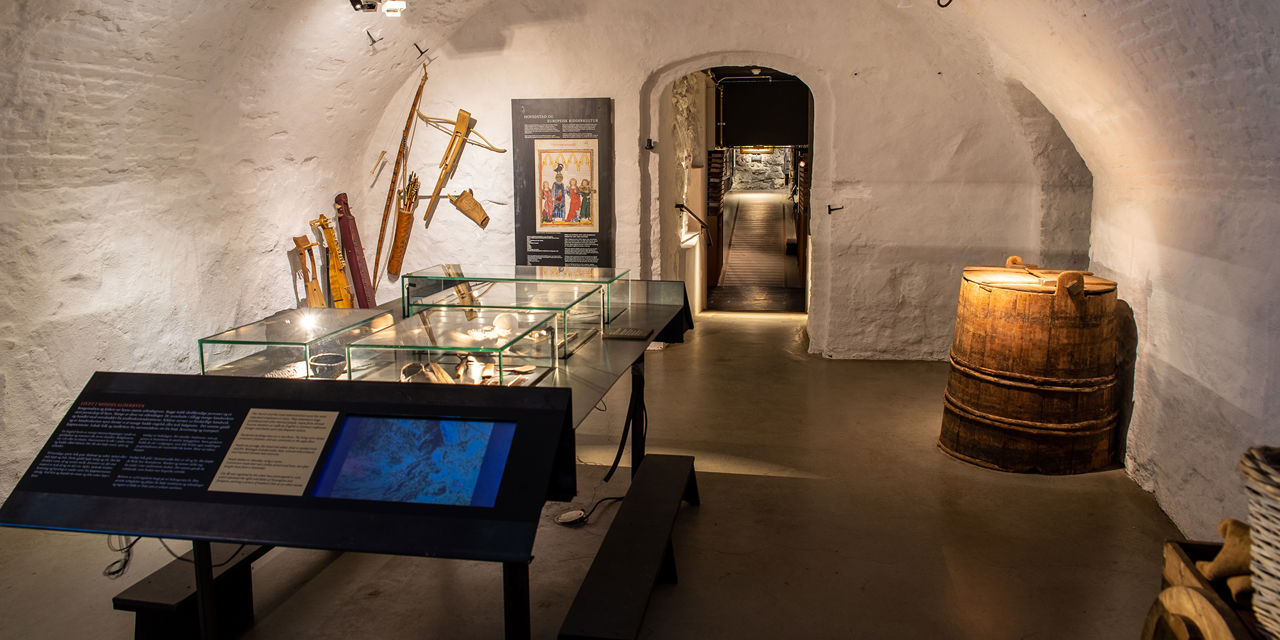Kjellerlokale i et museum, hvitmalte murvegger og et glassmonter med museumsgjenstander