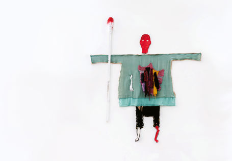 Tekstilkunst på vegg der en menneskefigur med rødt hode holder en stor bomullspinne med blod på.