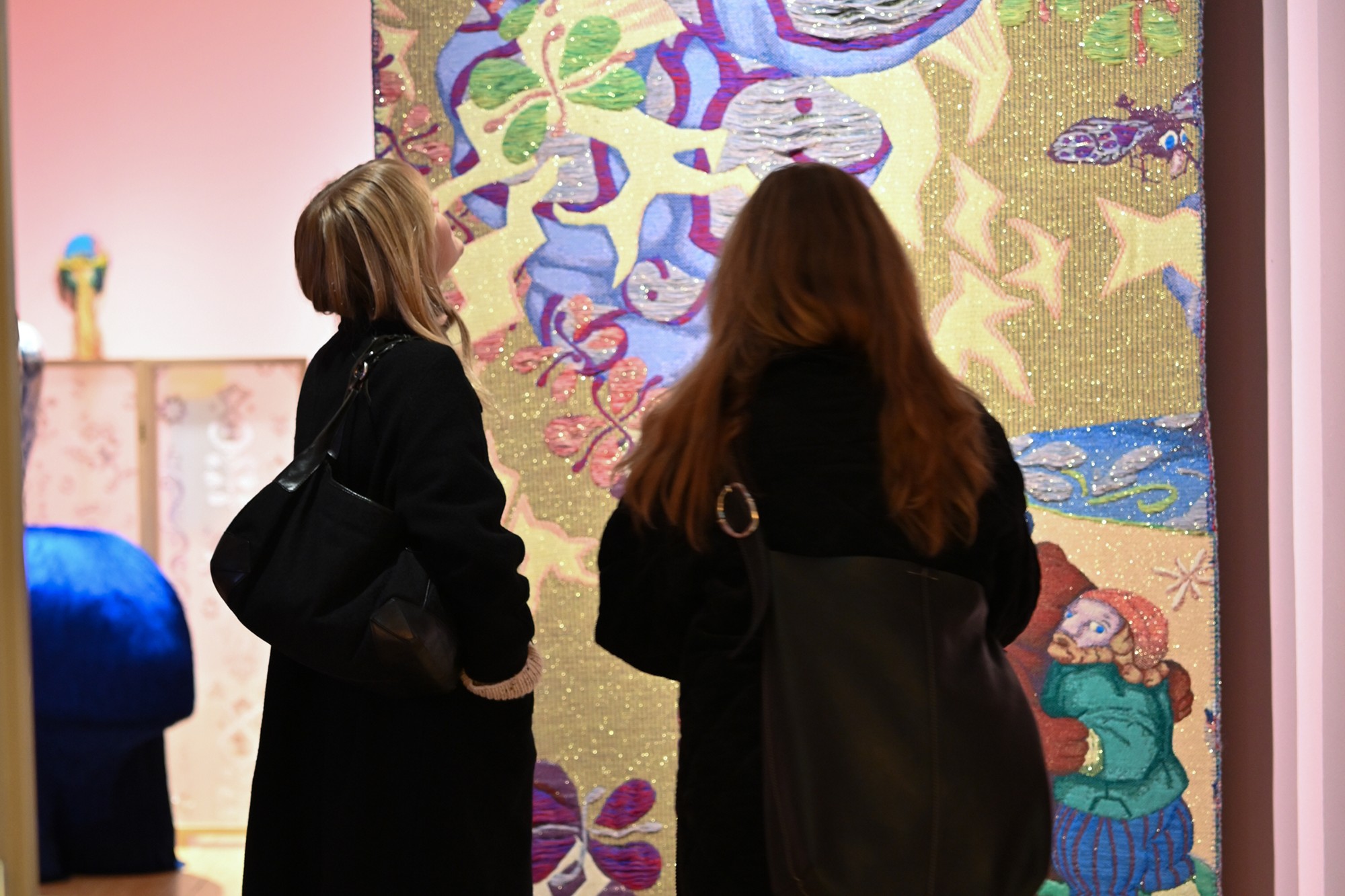 To kvinner står med ryggen til og ser på et fargerikt tekstilkunstverk