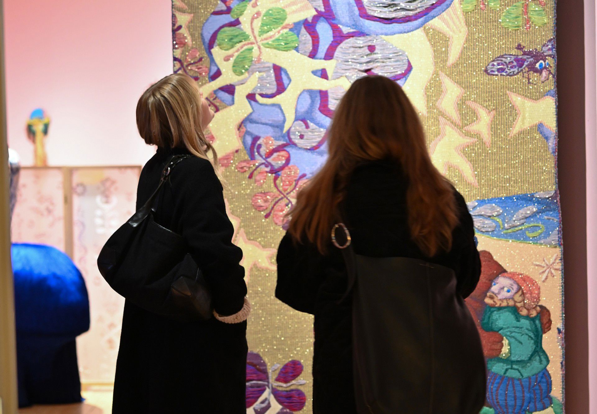 To kvinner står med ryggen til og ser på et fargerikt tekstilkunstverk